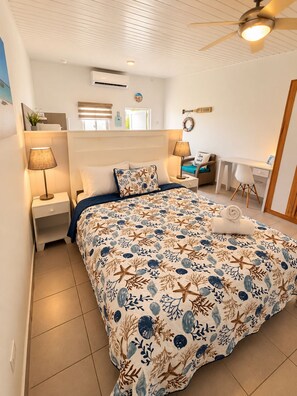 A bedroom with a bed, nightstands, a desk, and a ceiling fan. - Paradise Studio Aruba (Oranjestad)