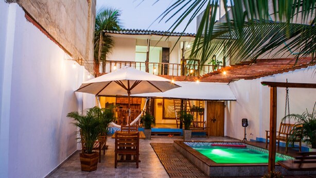 Un patio al aire libre con mobiliario de madera, sombrillas, una piscina pequeña y plantas en macetas.