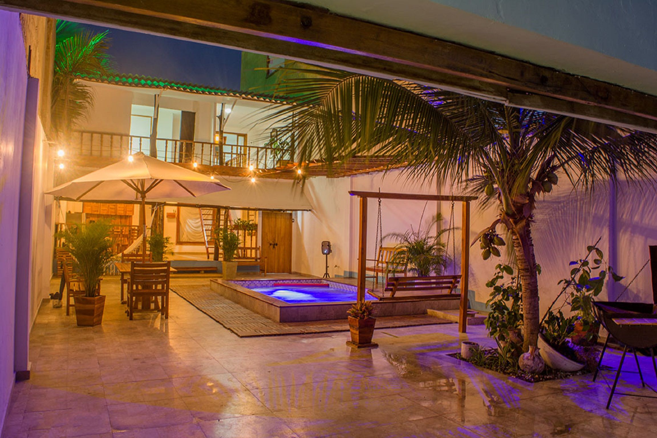 A spacious outdoor area with a pool, seating, and a swing set, surrounded by potted plants and palm trees.