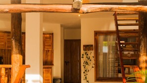 Una escalera de madera que lleva a una puerta, una planta y un ventanal con vista al interior.