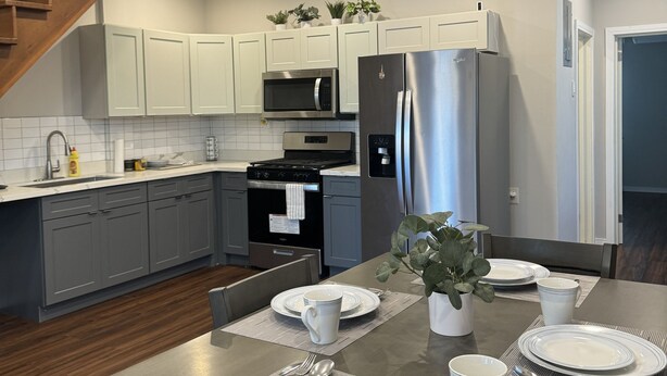 A modern kitchen with white cabinets, stainless steel appliances, and a dining area set for four. - A modern Townhome at Farm. 5 minutes drive from the Providence National Stadium (East Bank Demerara)
