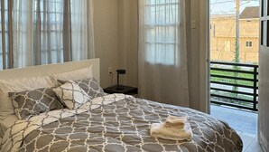 A bedroom with a large bed, a bedside table with a lamp, and a view of the outside balcony. - A modern Townhome at Farm. 5 minutes drive from the Providence National Stadium (East Bank Demerara)