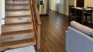 A wooden staircase leading to a living area with a kitchen in the background.