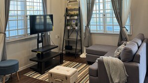 A modern living room with a flat-screen TV, grey sofa, and a small ottoman. - A modern Townhome at Farm. 5 minutes drive from the Providence National Stadium (East Bank Demerara)