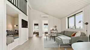 Un vaste espace de vie doté d’un plafond haut, de lambris en bois, d’une grande fenêtre et d’un coin salon confortable.