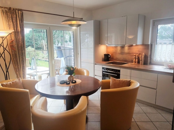 Una cocina moderna con una mesa redonda y sillas, horno empotrado y ventana con vistas a un jardín.