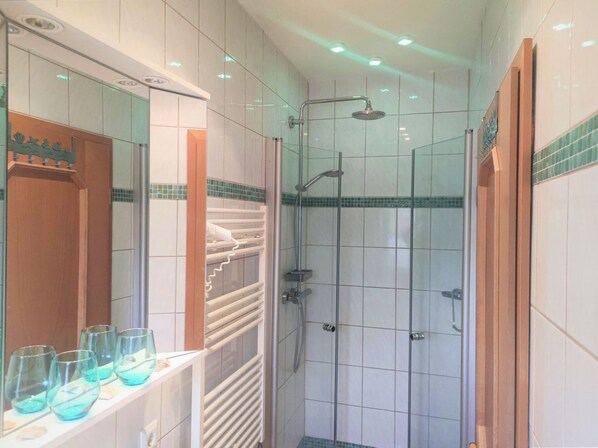 A modern bathroom with a glass shower enclosure, a vanity with a mirror, and a shelf with glasses. - F-1064 Rhododendronblüte - Ferienwohnung Rhododendronblüte F-1064 Wohnung 01 (Lietzow)