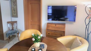 A dining area with a round table, chairs, a vase with flowers, and a television on the wall.