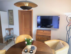 Una zona de menjador amb taula rodona, cadires, un ram de flors i un televisor a la paret.