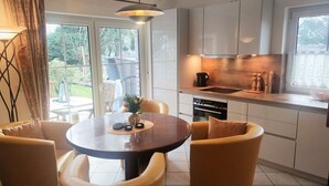 A modern kitchen with a round dining table and chairs, a built-in oven, and a window overlooking a garden.