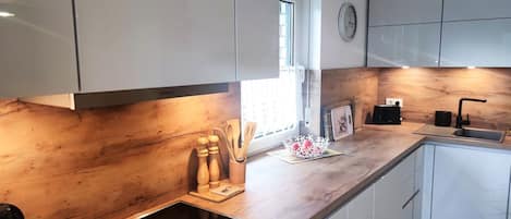 A modern kitchen with white cabinets, a wooden countertop, a built-in stove, and a window providing natural light.