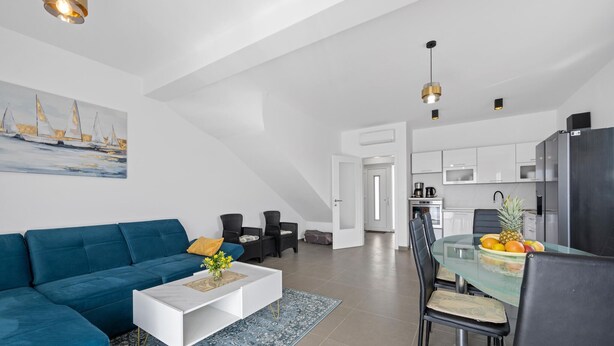 A modern living room with a blue sofa, a white coffee table, and a dining area with a glass table and chairs. - Amazing home in Vodice with WiFi (Vodice)