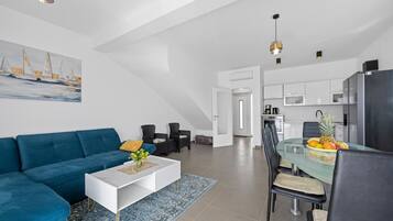A modern living room with a blue sofa, a white coffee table, and a dining area with a glass table and chairs.