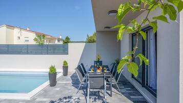 A patio with a pool, a table set for two with drinks, and potted plants.