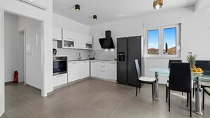 A modern kitchen with white cabinetry, a black refrigerator, and a dining area with a glass table and chairs. - Amazing home in Vodice with WiFi (Vodice)