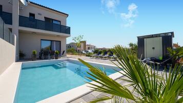 A swimming pool with lounge chairs, a small building, and a two-story house with balconies.