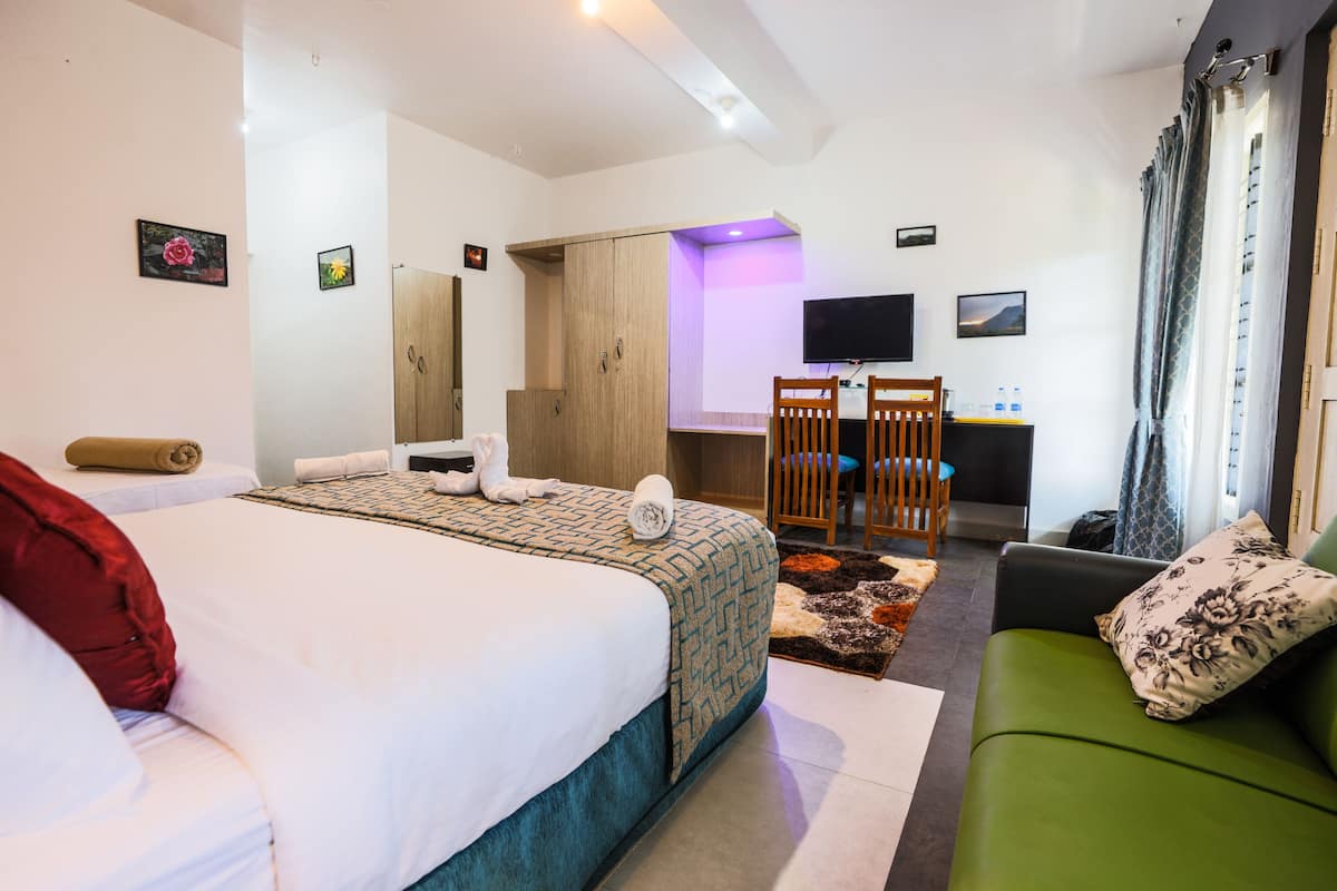 Quarto de hotel com cama, sofá verde, escrivaninha com cadeira, televisão e guarda-roupa.