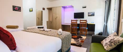 A hotel room with a bed, a green sofa, a desk with a chair, a TV, and a wardrobe.