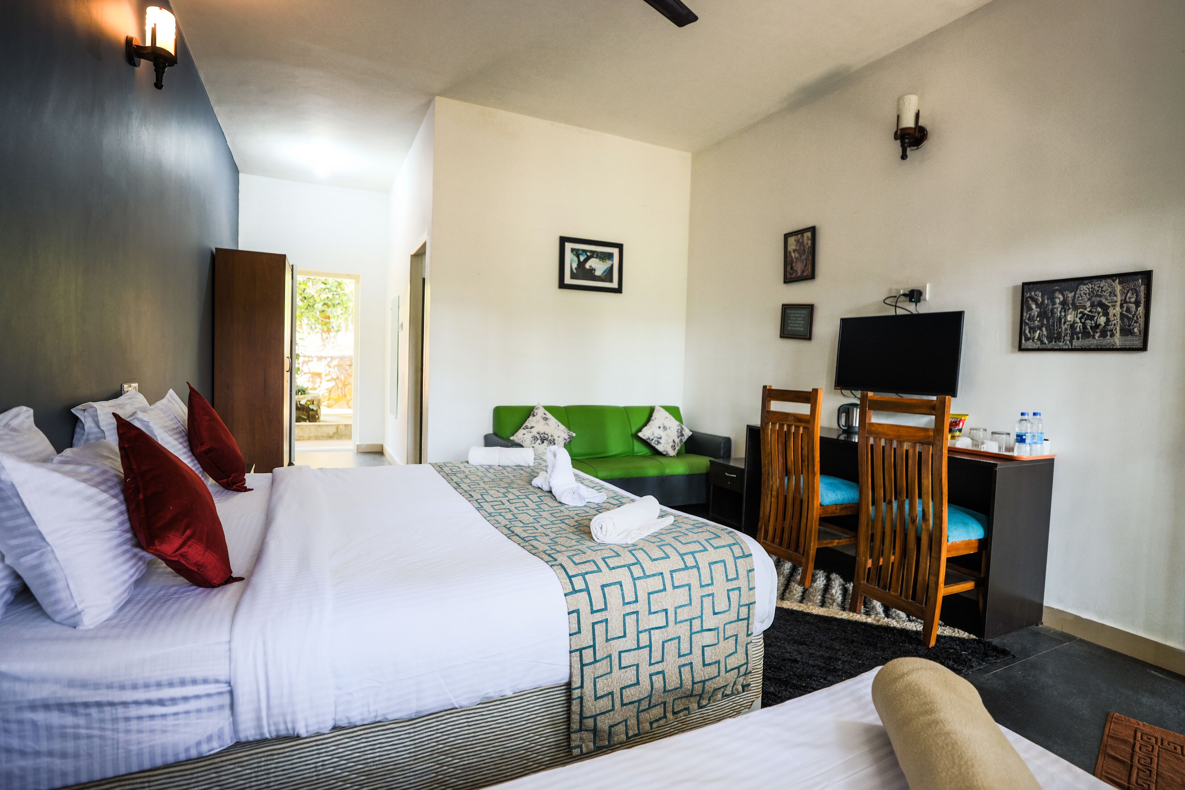 Une chambre d’hôtel avec un grand lit, un canapé vert, un bureau avec une télévision et une fenêtre donnant sur un beau paysage.