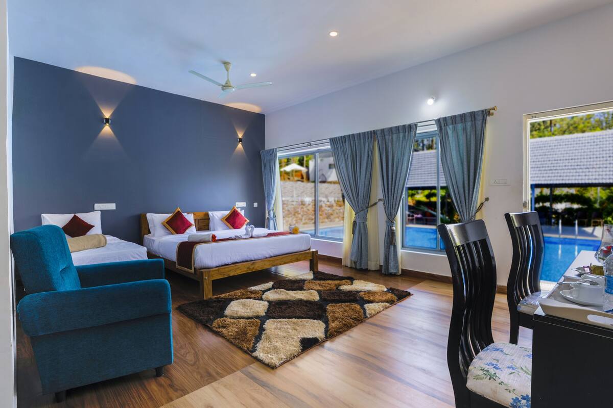 Quarto de hotel moderno com duas camas, área de refeições e vista para uma piscina.