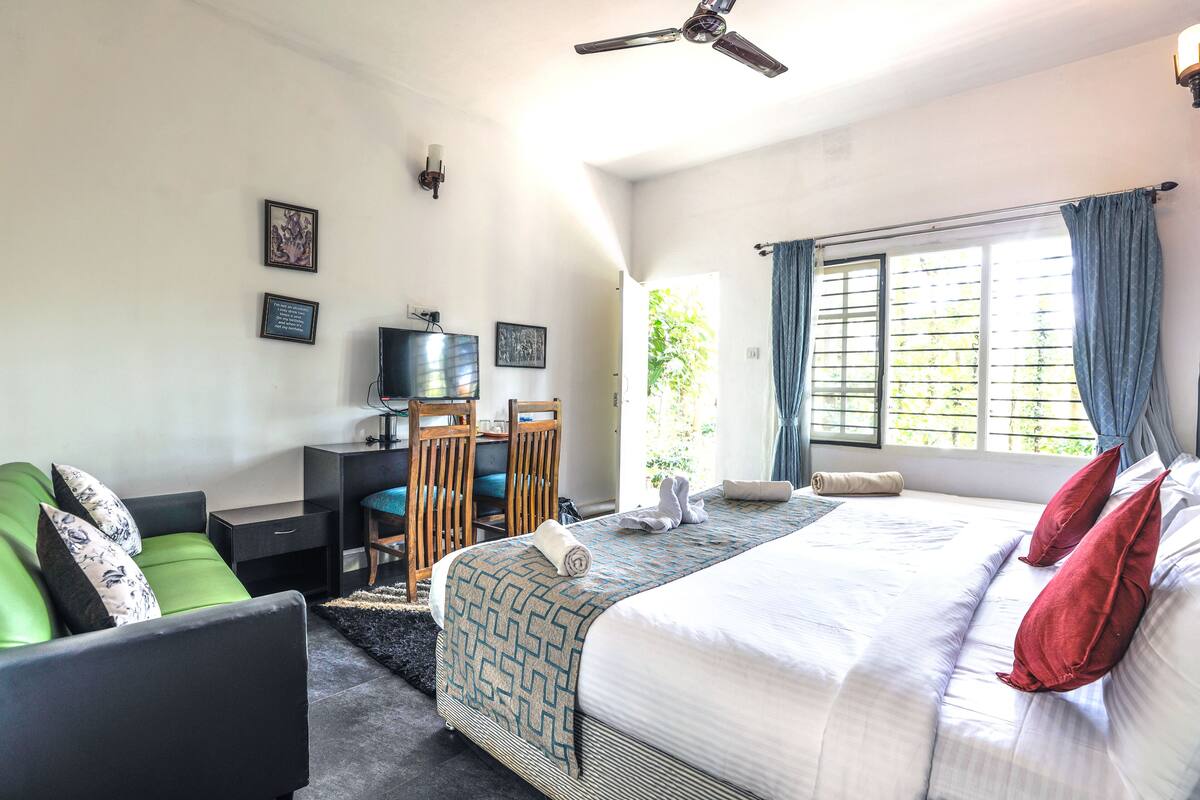 Quarto de hotel com cama, escrivaninha, cadeira e televisão.