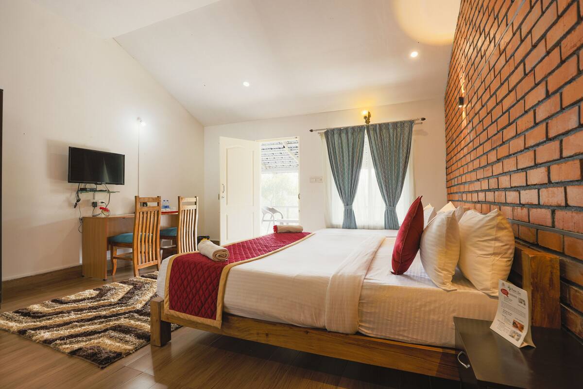 Quarto com cama de madeira, uma escrivaninha, uma cadeira, televisão e parede de tijolos.