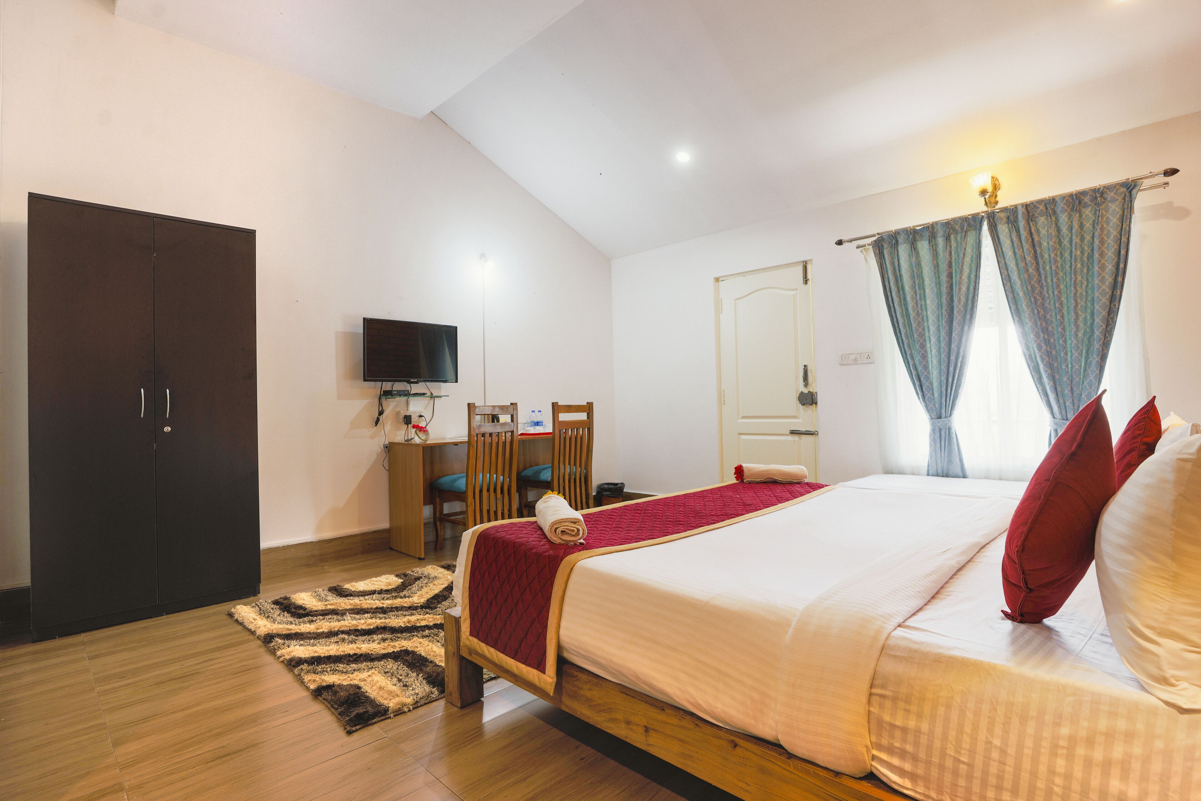 A bedroom with a large bed, a desk, a chair, a wardrobe, and a television.