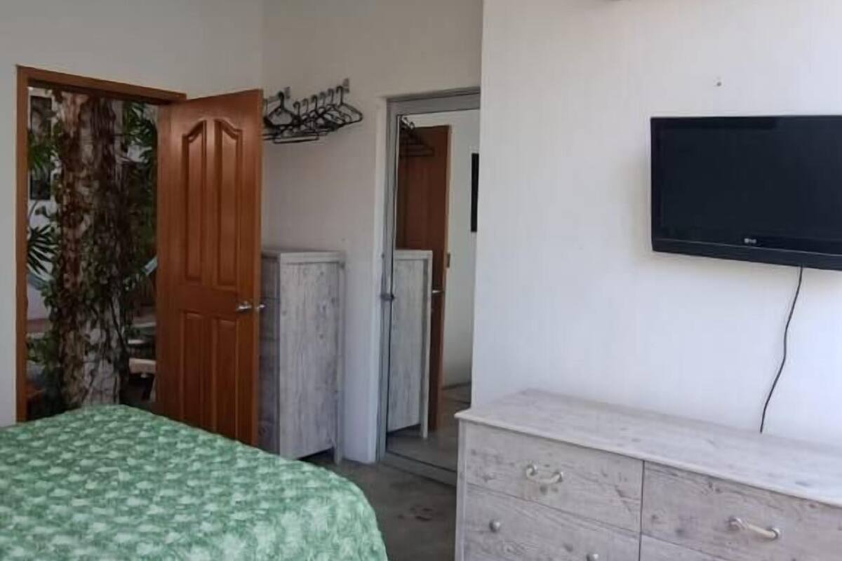 A bedroom with a bed, a dresser, a television, and an air conditioning unit.
