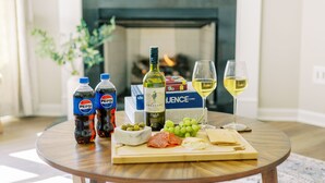 A round wooden table with a variety of food items, including cheese, grapes, and meat, along with bottles of Pepsi and a bottle of wine. - Amazing 3 BR Home | 5 mins to DT | Pet Friendly (New Bern)