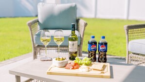A table with a bottle of wine, two glasses of white wine, a bottle of Pepsi, a bowl of olives, a plate of cheese and salami, and a plate of grapes. - Amazing 3 BR Home | 5 mins to DT | Pet Friendly (New Bern)
