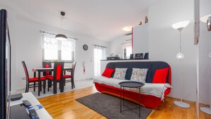 Una sala de estar moderna con un sofá rojo y negro, una mesa de comedor con sillas, una mesita redonda y un televisor.