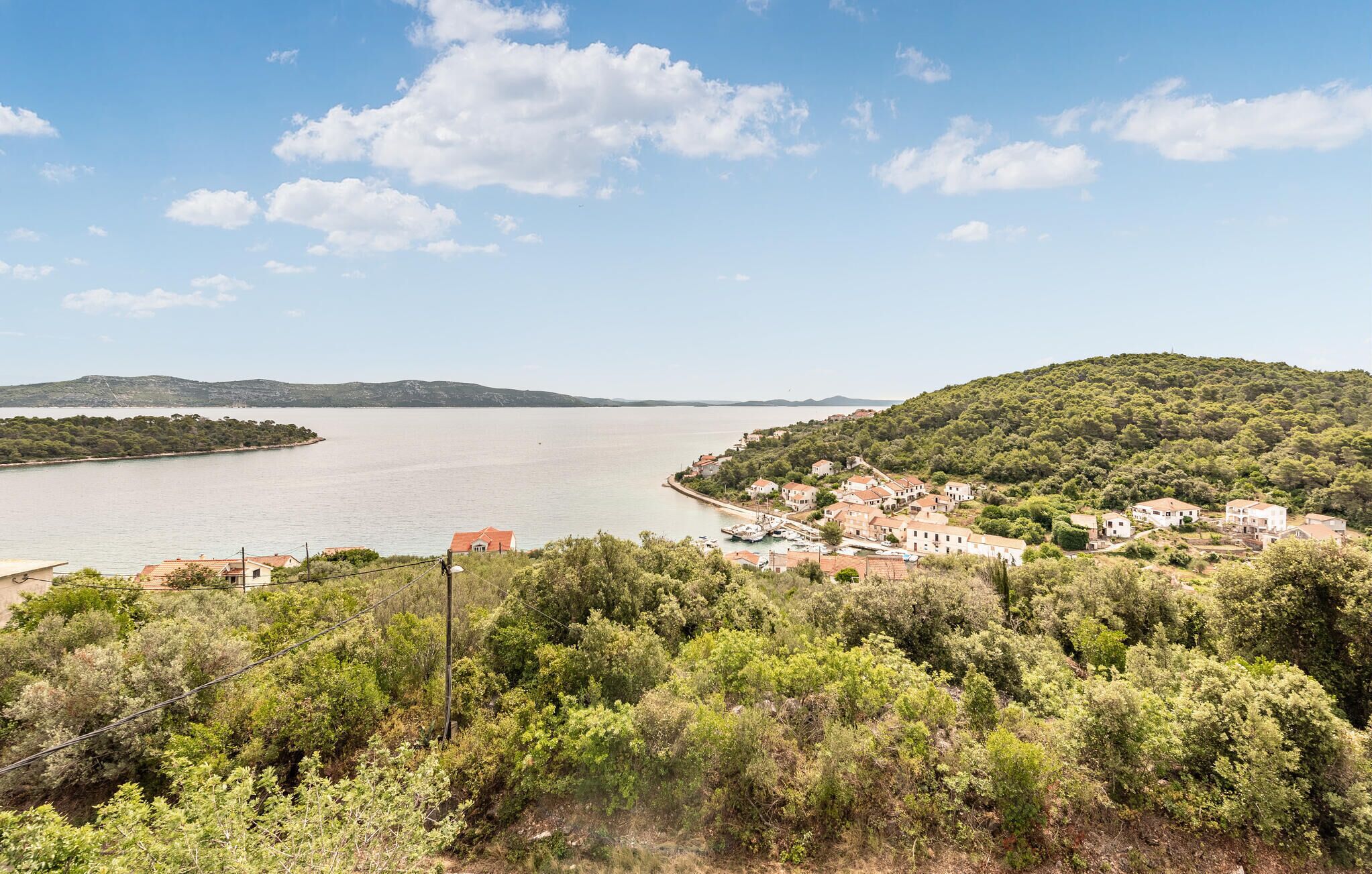 A coastal town with houses near the water, surrounded by greenery and hills.