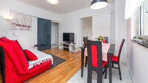 Una sala de estar moderna con un sofá rojo, una mesa de comedor con sillas, un televisor y una puerta de cristal que da al baño.