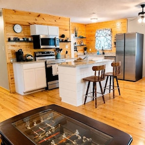 A kitchen with wooden walls, a central island, bar stools, a refrigerator, and a foosball table.