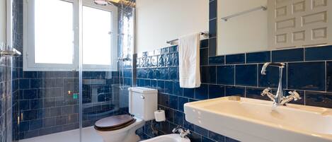 A modern bathroom with a glass-enclosed shower, a toilet with a wooden seat, a bidet, and a large sink with a mirror above it.