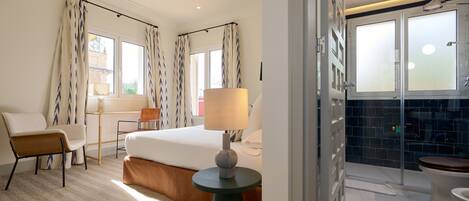 Une chambre d’hôtel comprenant un lit, un bureau, une chaise, une lampe, ainsi qu’une salle de bain avec douche et toilettes.