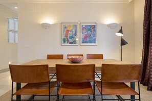 Uma sala de jantar com uma mesa de madeira, cadeiras marrons, duas obras de arte emolduradas e um abajur.