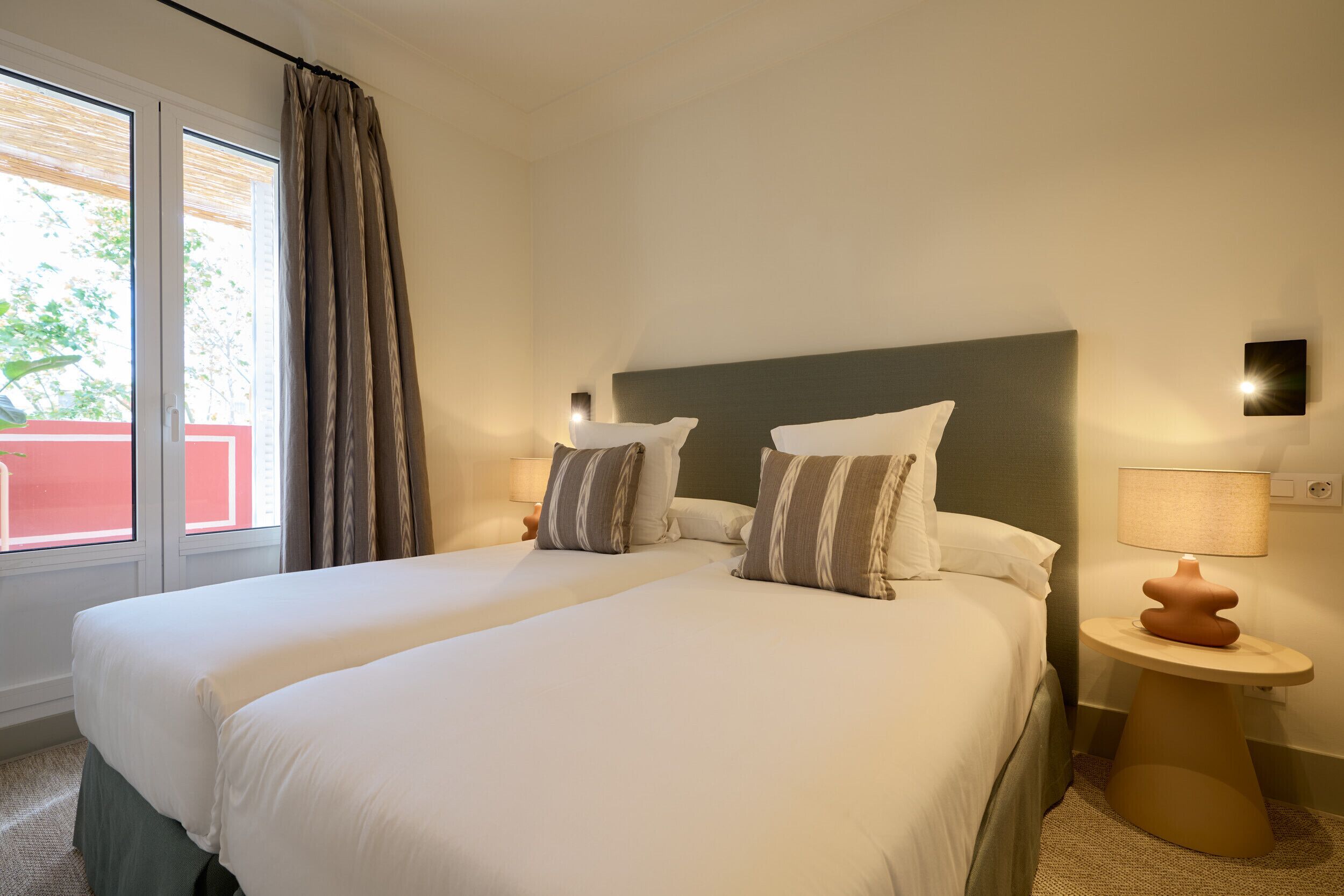 A double bed with two pillows, a bedside table with a lamp, and a window with curtains.