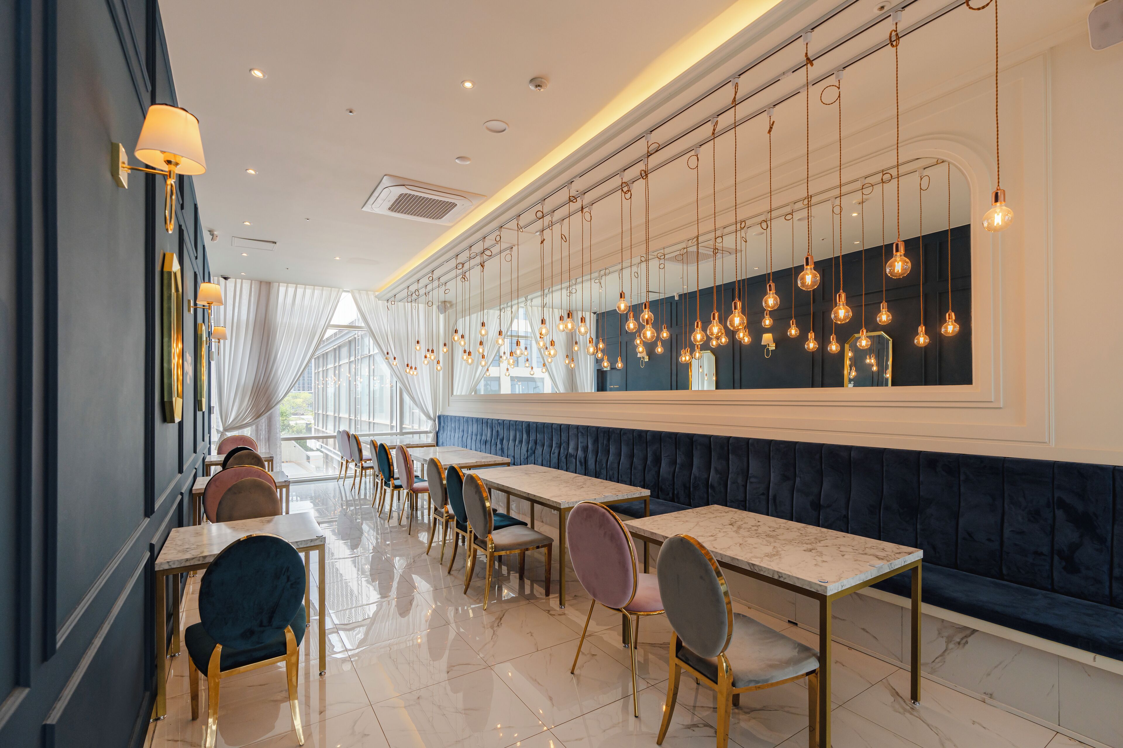 Un interior de restaurante moderno con mesas de superficie de mármol, sillas tapizadas y lámparas colgantes.