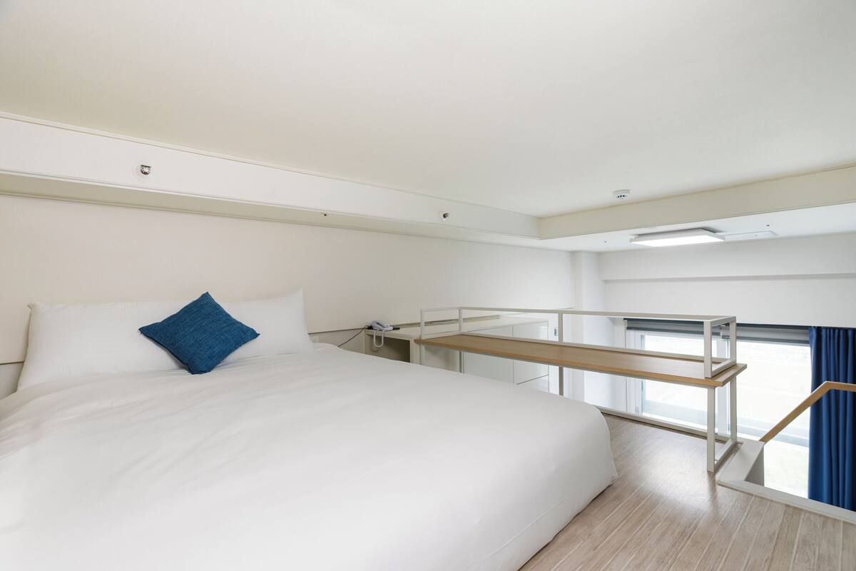 A modern hotel room with a large bed, a small desk, and a window with curtains.