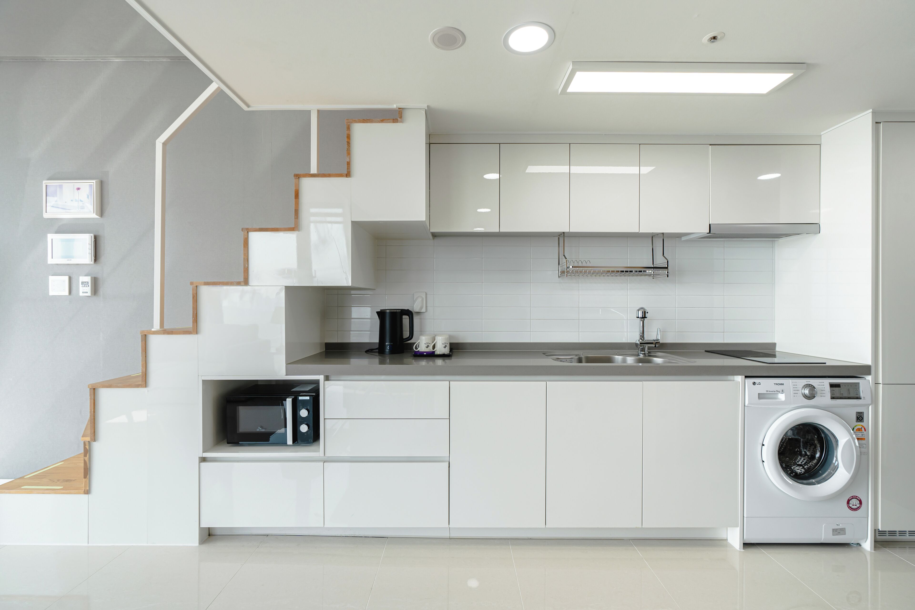 A modern kitchen with white cabinetry, a built-in microwave, a coffee maker, and a washing machine.