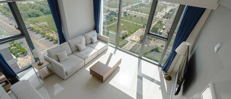 Una sala de estar moderna con un sofá blanco, una mesa de centro y vistas a un paisaje urbano a través de ventanas grandes.