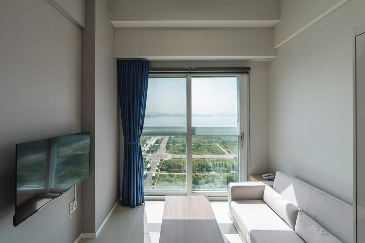 A modern living room with a flat-screen TV, a sofa, and a large window offering a city view.