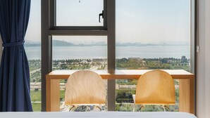 A room with a large window, two wooden chairs, a wooden desk, and a view of a body of water and distant landscape. - SR Hotel Yeongjong (Incheon)
