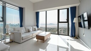 A modern living room with a white sofa, a wooden coffee table, and a large window with a city view. - SR Hotel Yeongjong (Incheon)