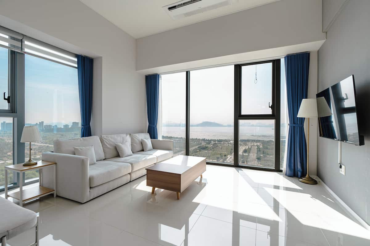 A modern living room with a white sofa, a wooden coffee table, and a large window with a city view.