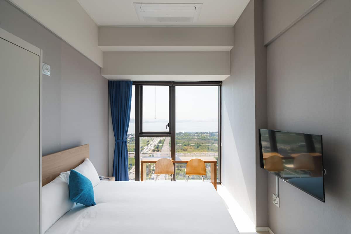 A hotel room with a large bed, a TV mounted on the wall, and a balcony with two chairs and a table.