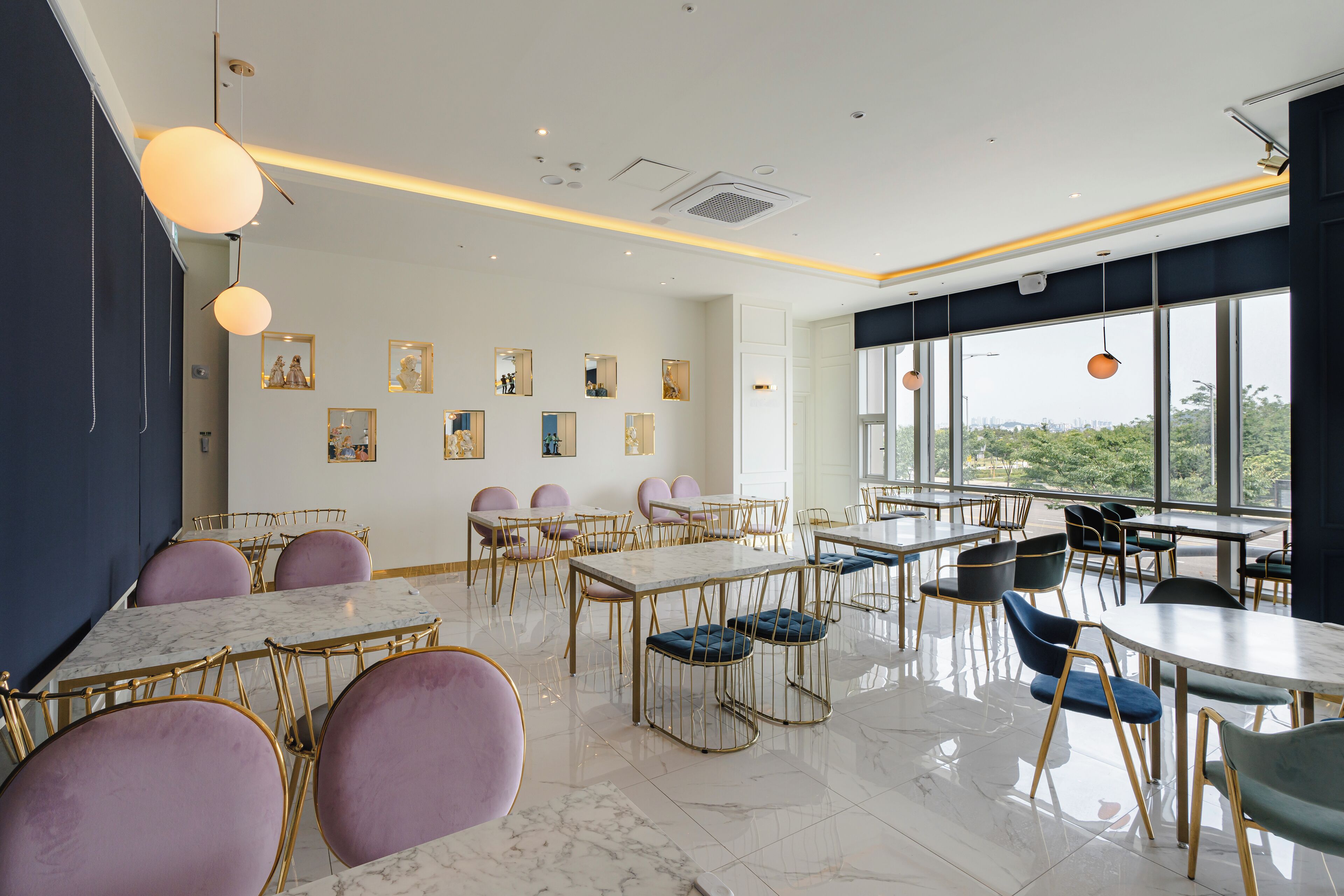 A modern dining area with marble tables and chairs, large windows offering a view, and artwork on the walls.