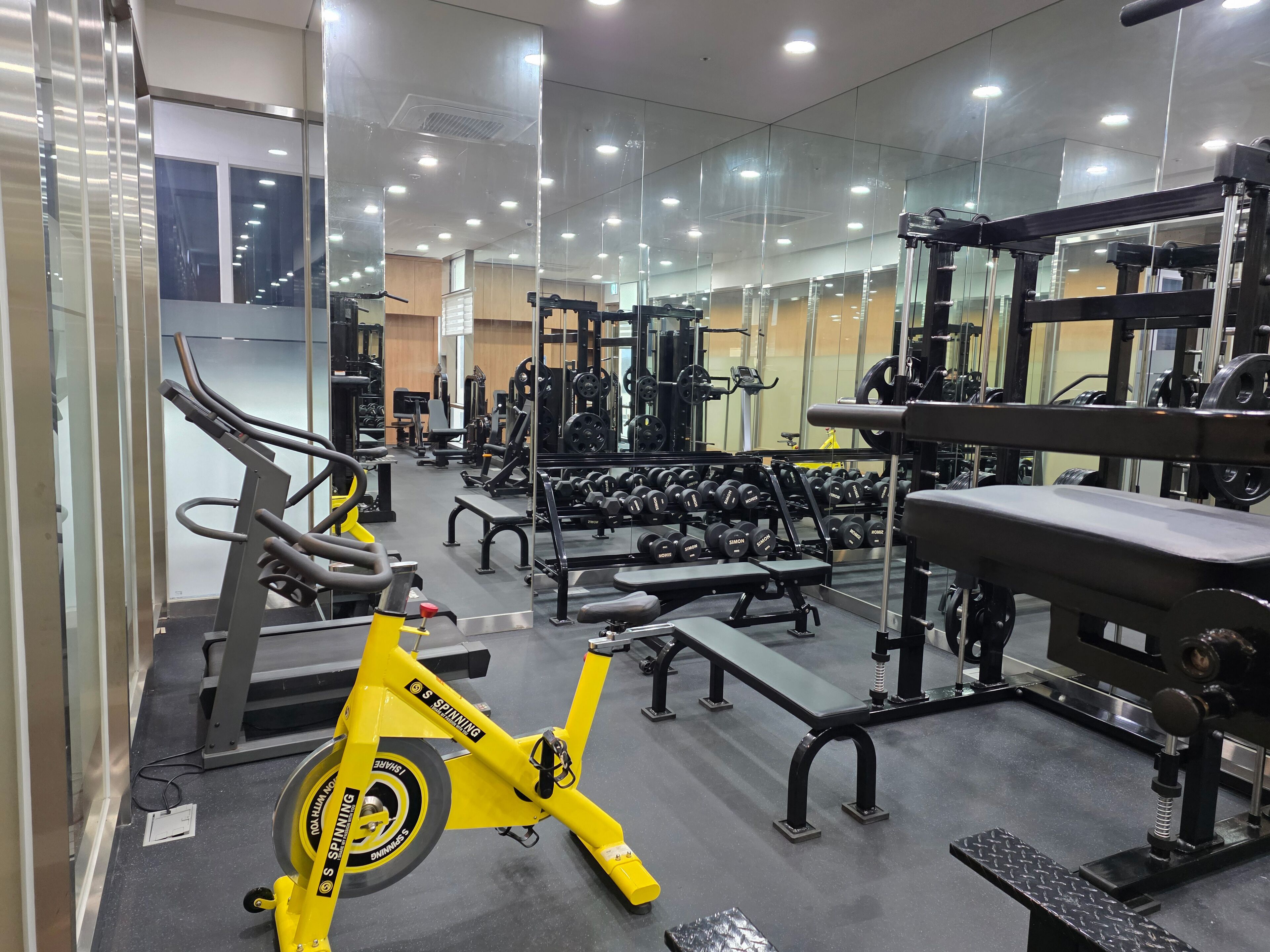 A gym with various exercise equipment, including a yellow spinning bike, benches, and weight machines.
