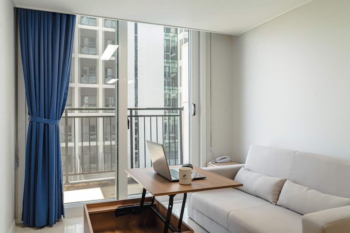 A modern living room with a white sofa, a wooden table with a laptop, and a blue curtain.